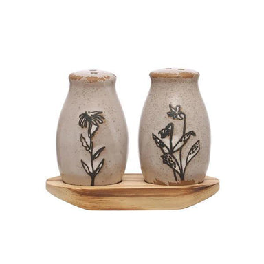 Two ceramic salt and pepper shakers with floral designs on a wooden tray against a white background.