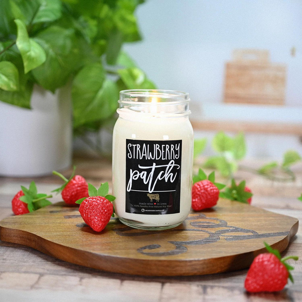 Candle labeled 'Strawberry Patch' on a wooden board with strawberries and a plant in the background