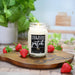 Candle labeled 'Strawberry Patch' on a wooden board with strawberries and a plant in the background