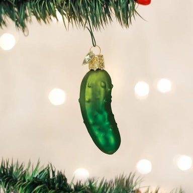 Green pickle ornament hanging on a Christmas tree with lights in the background