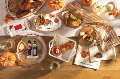 Thanksgiving table setting with roasted turkey, pumpkins, and decorative plates on a wooden table.