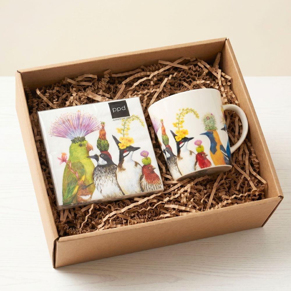 Two mugs with bird designs in a cardboard box with straw padding.