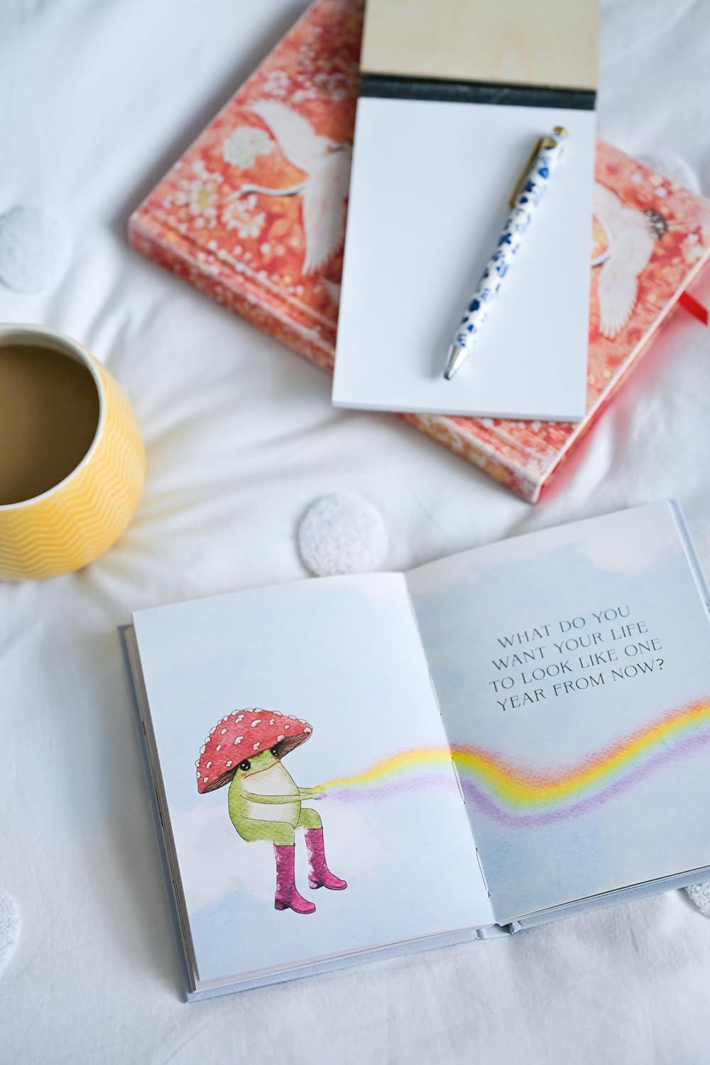 Open book with a child in a raincoat and umbrella illustration, on a light surface with a mug and notebook.