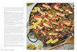 Paella dish with vegetables and lemon wedges on a white surface