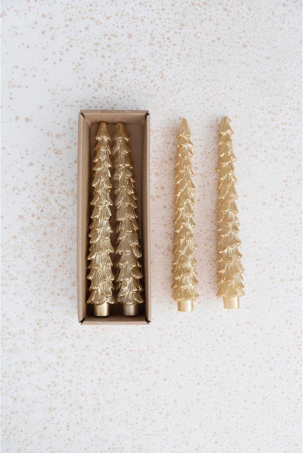 Set of gold tree-shaped candles with one outside the box on a textured white background