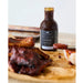 Bottle of vidalia onion BBQ sauce on a wooden cutting board with ribs and a brush.