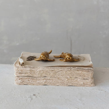 Two small bronze sculptures of seals on a stack of textured paper against a gray background