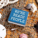 Blue sign with 'WE'RE BEACH PEOPLE' text on a netting background with shells.