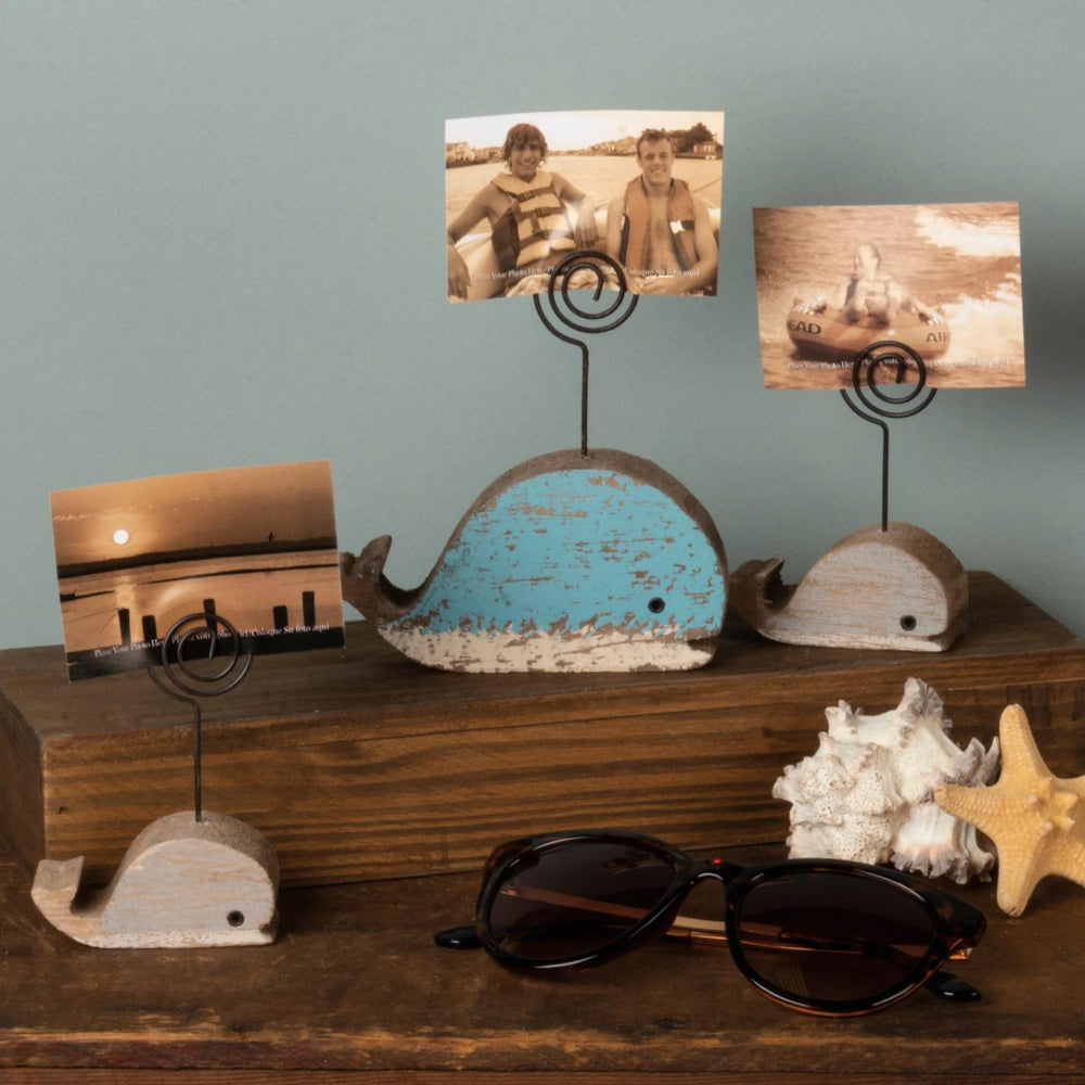 Wooden whale-shaped photo holders with photos on a wooden surface against a gray wall.