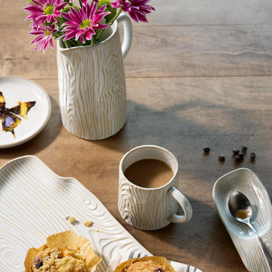 Cup of coffee with a muffin, flowers, and a butterfly on a wooden table.