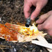 Person using a fire starter to ignite wood on a natural ground surface