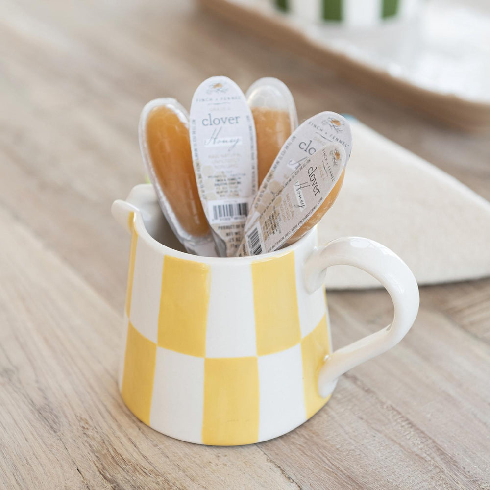Yellow and white checkered mug with clover brand sewing notions on a wooden surface