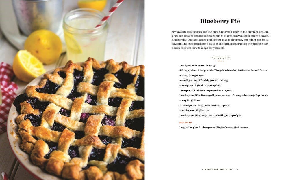 Blueberry pie with lemons and a glass of lemonade on a table, next to a recipe card for Blueberry Pie.
