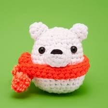 A white crocheted polar bear amigurumi toy wearing a bright orange-red knitted scarf, set against a solid green background.