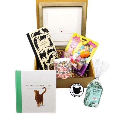 This gift box is filled with cat-themed goodies, including a bag of premium chocolate truffles, a mug, a journal, a beautifully framed art piece, the book "When You Love a Cat” and cat squishies.